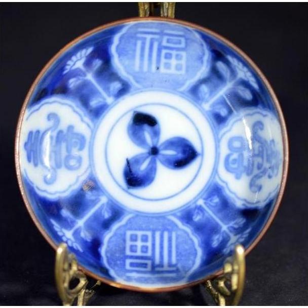 Blue and white hand painted ceramic Asian plate with Chinese characters on brass stand, close-up view.
