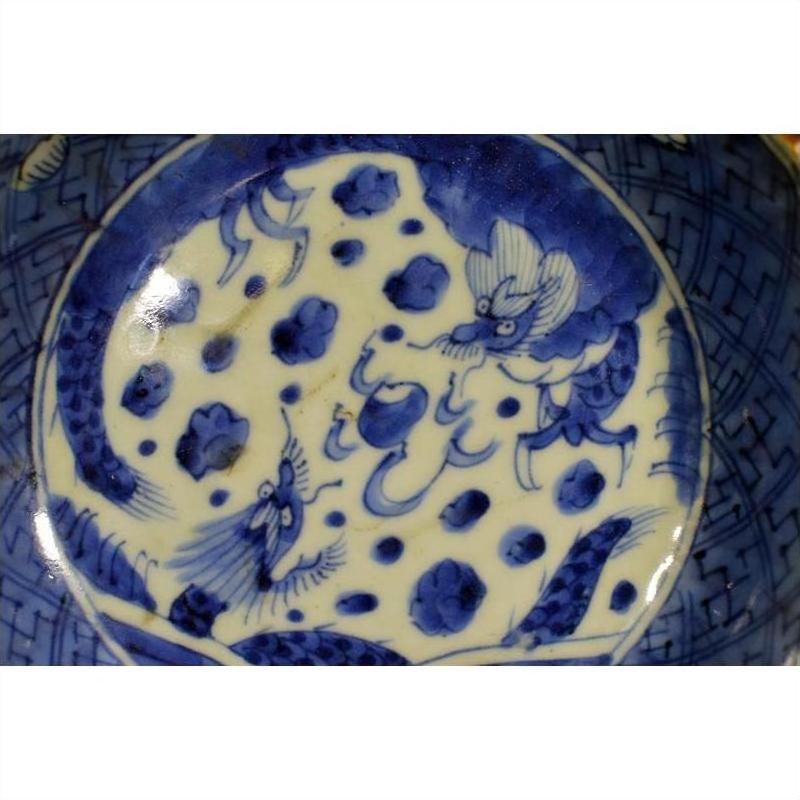 Close-up of blue and white ceramic Chinese bowl with hand painted dragon and cloud design in central circle.