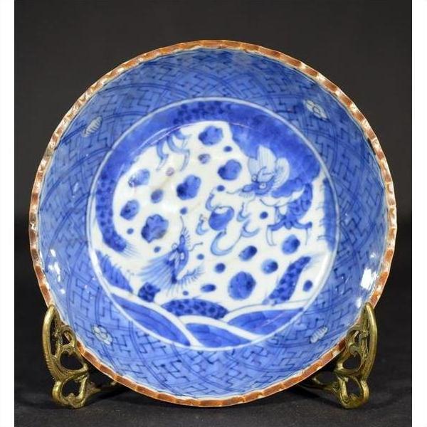 Close-up of an antique hand painted Chinese ceramic bowl with dragon and cloud motifs on a brass stand, dark background.