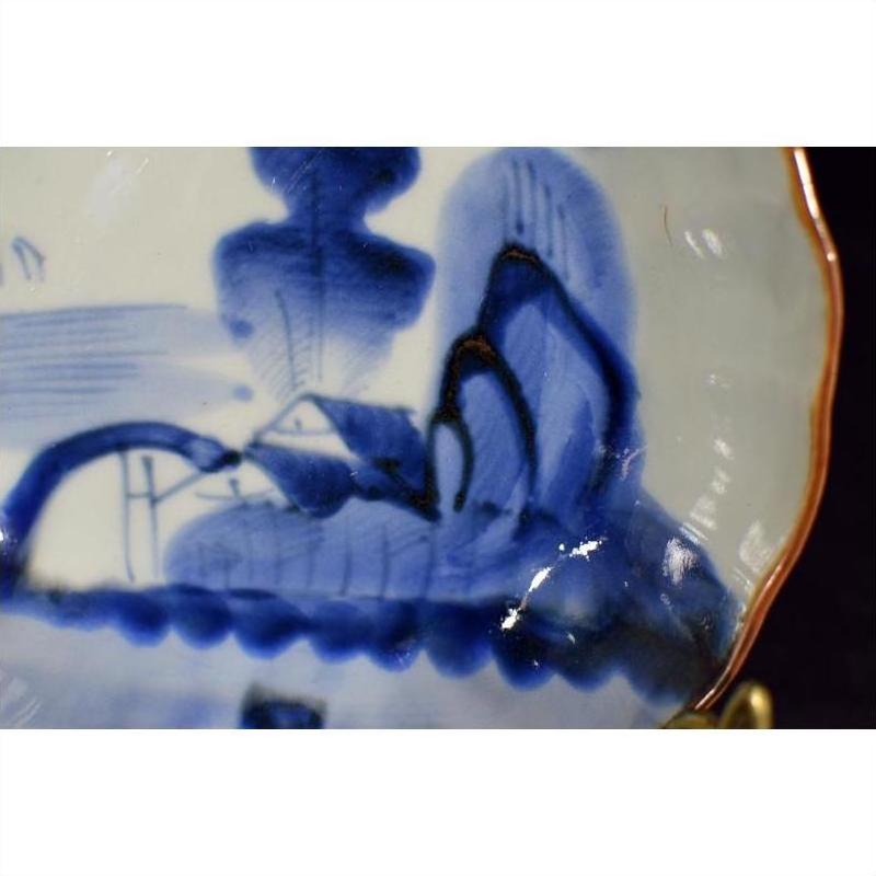 Close-up of blue and white hand painted porcelain bowl with scalloped edge, featuring Chinese landscape design.