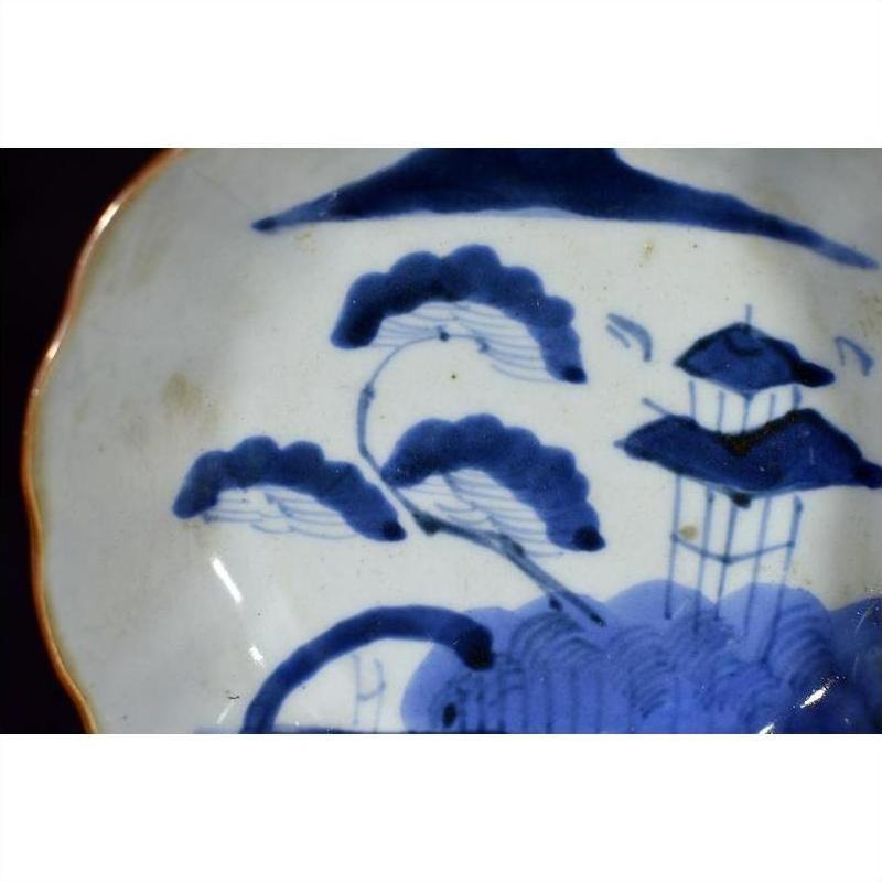 Blue and white porcelain plate with hand painted landscape, trees, and pagoda, close-up view.