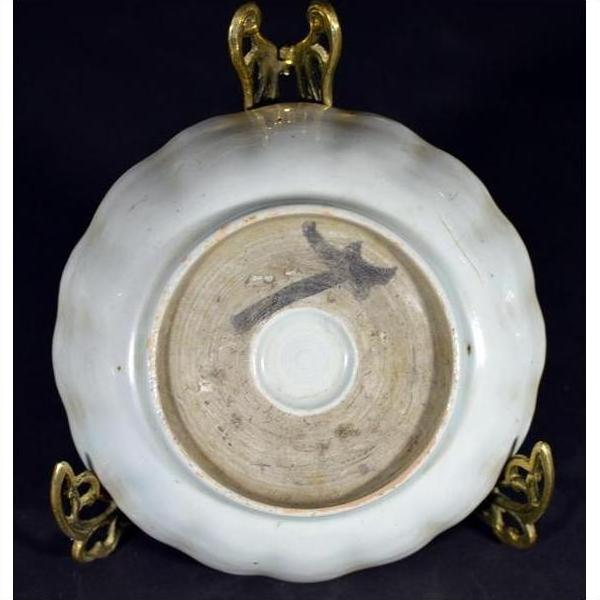 Close-up of the underside of an antique hand painted Chinese porcelain plate on a brass stand against a dark background.