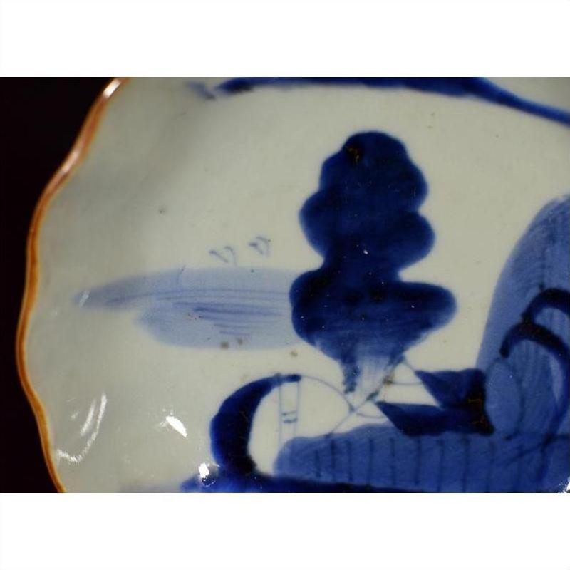 Close-up of blue and white hand-painted antique Chinese porcelain plate with orange rim on dark background.