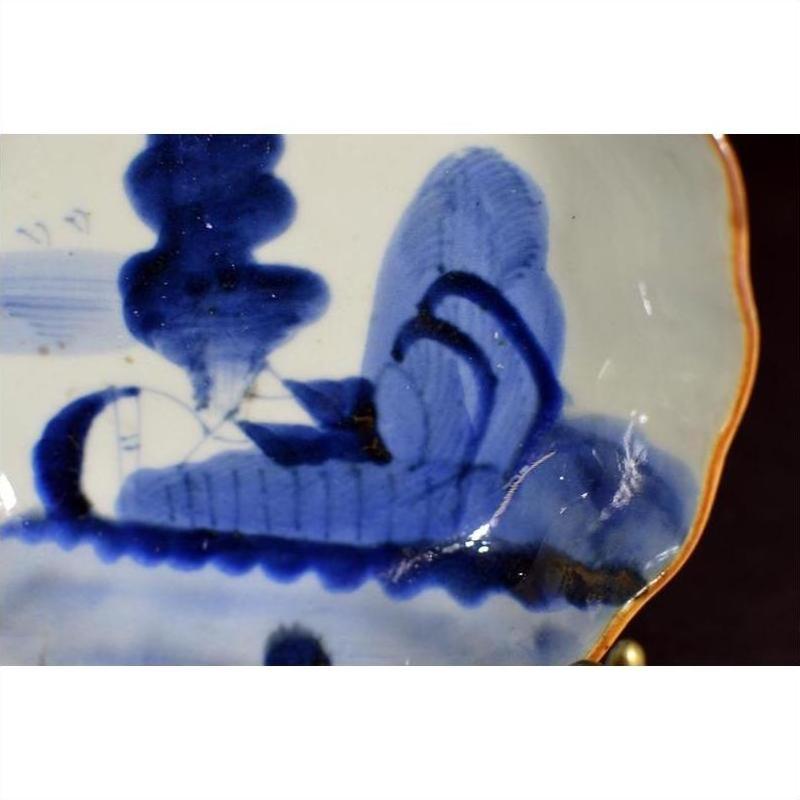 Close-up of blue and white porcelain plate with gold-trimmed wavy edge and hand painted abstract design.