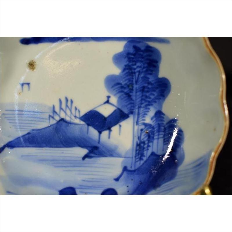 Blue and white porcelain plate with hand-painted Chinese landscape, trees, house, and fence, close-up view.