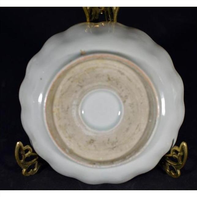 Close-up of an antique hand-painted Chinese porcelain plate with scalloped edge on a brass stand, black background.