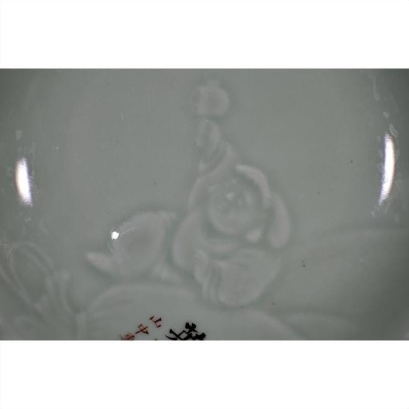 Close-up of antique hand-painted embossed Japanese plate, glossy ceramic with smiling robed figure holding object.