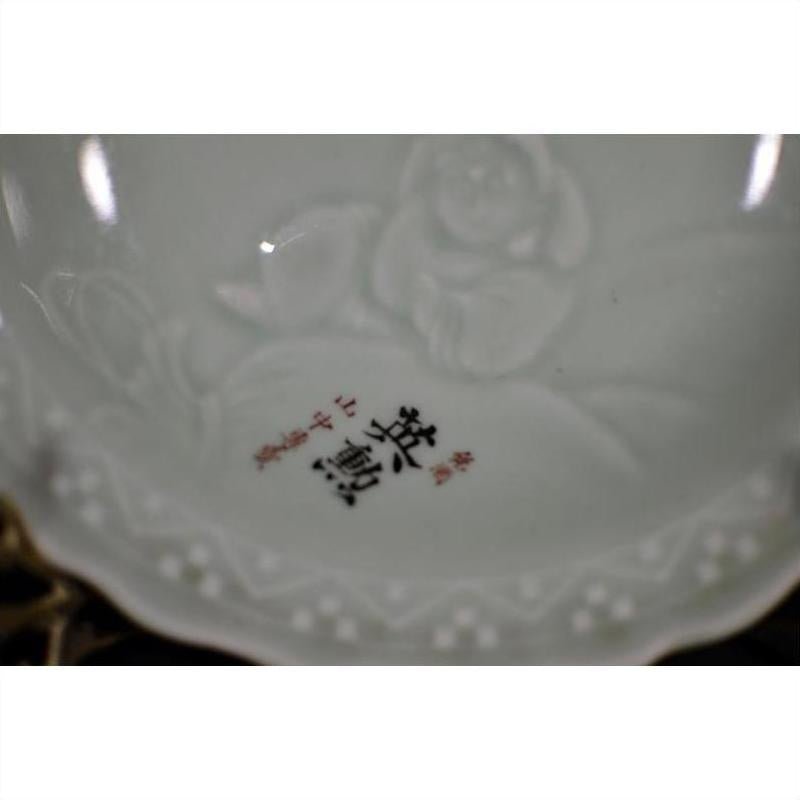 Close-up of antique hand painted embossed Japanese porcelain plate with red characters and unique art in the center.