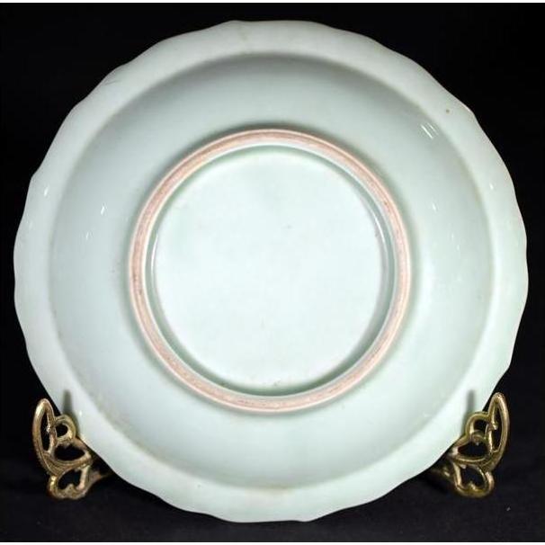 Close-up of antique hand painted embossed Japanese plate with faint pink ring on gold stand against black background.