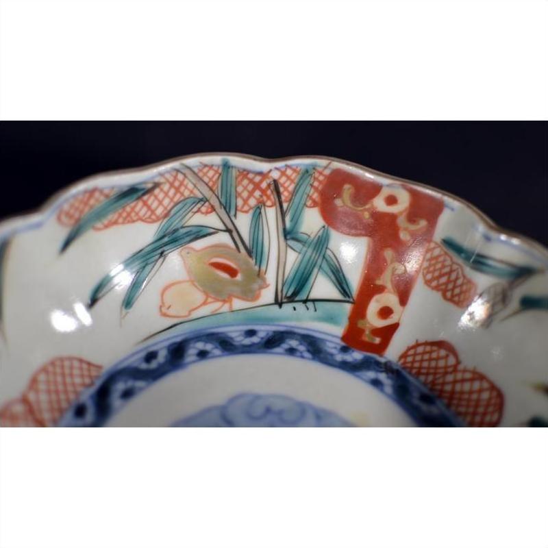 Close-up of a multicolored porcelain Japanese Imari bowl with hand painted vibrant floral designs on the scalloped rim.