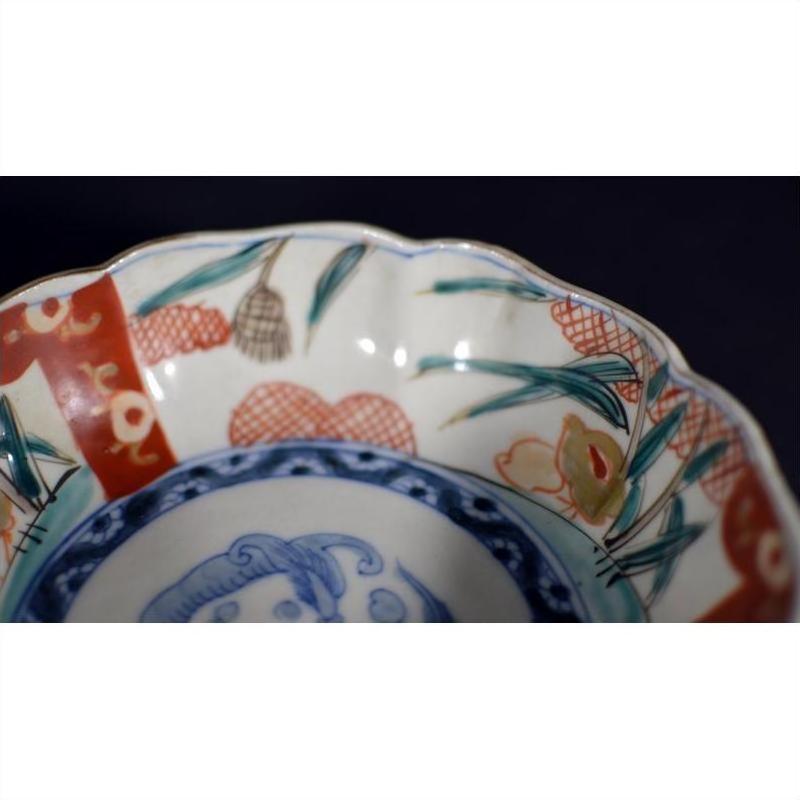 Close-up of blue, red, and green hand painted porcelain Imari bowl with scalloped edge and floral fruit rim motifs.