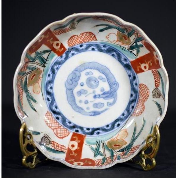 Close-up of an antique Japanese Imari porcelain bowl with red, green, and blue floral patterns on a brass stand.