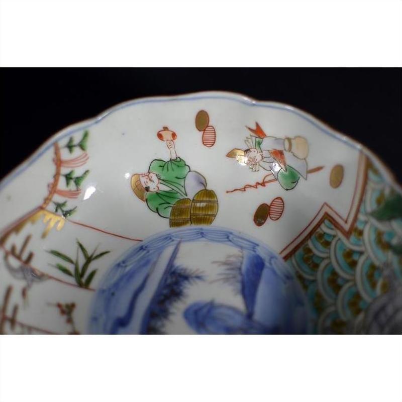 Close-up of antique Japanese Imari porcelain bowl with green and red figures, blue landscape details inside.