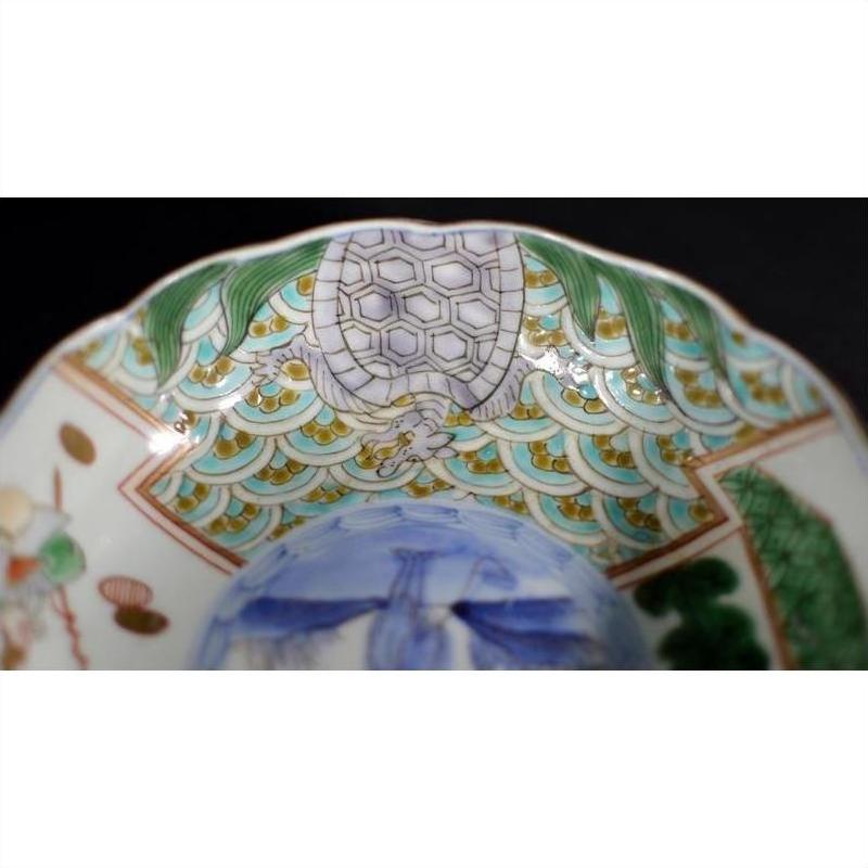 Close-up of a green and gold hand painted Japanese Imari porcelain bowl with turtle motif and ornate rim.