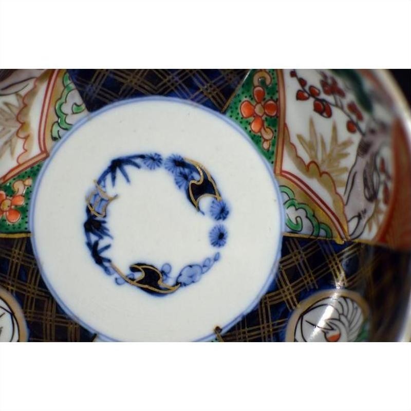 Close-up of blue, red, green, and gold hand painted floral patterns on antique Japanese Imari porcelain bowl.