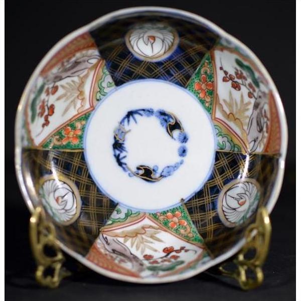 Vibrant multicolor hand painted Japanese Imari porcelain bowl on brass stand against dark background, close-up view.