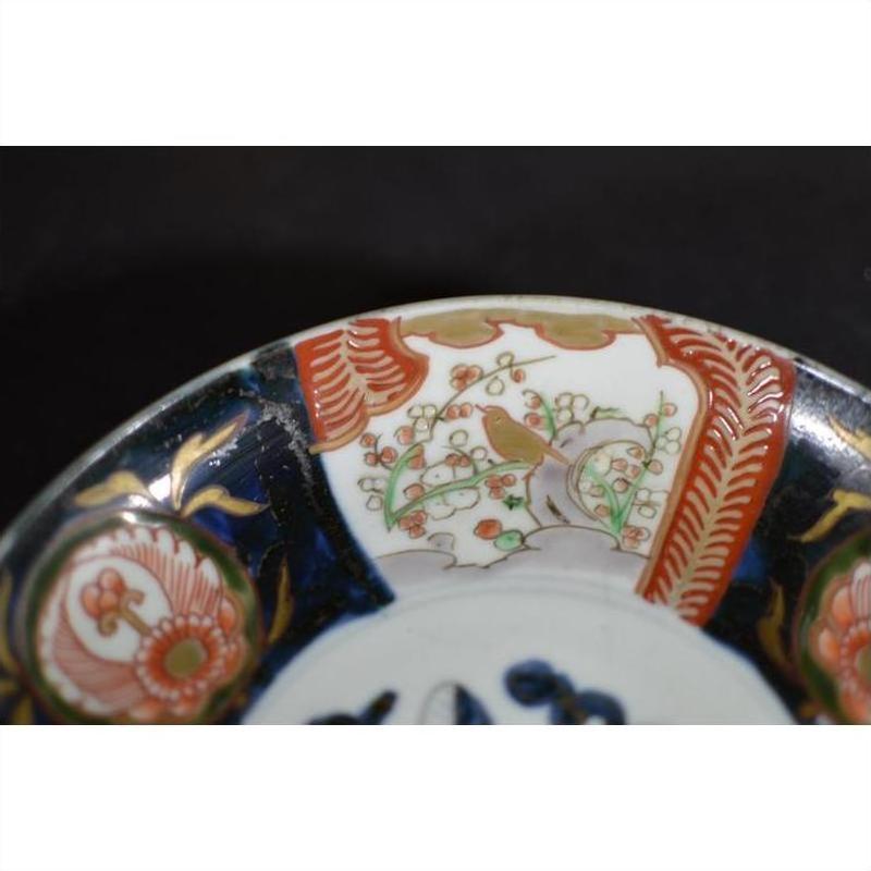 Close-up of red, green, and gold hand painted porcelain Japanese Imari bowl rim with floral and bird designs.