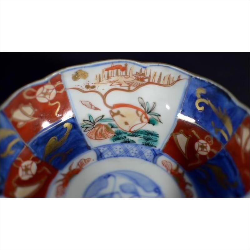 Close-up of red, blue, and gold porcelain Japanese Imari bowl with hand painted floral and landscape design.