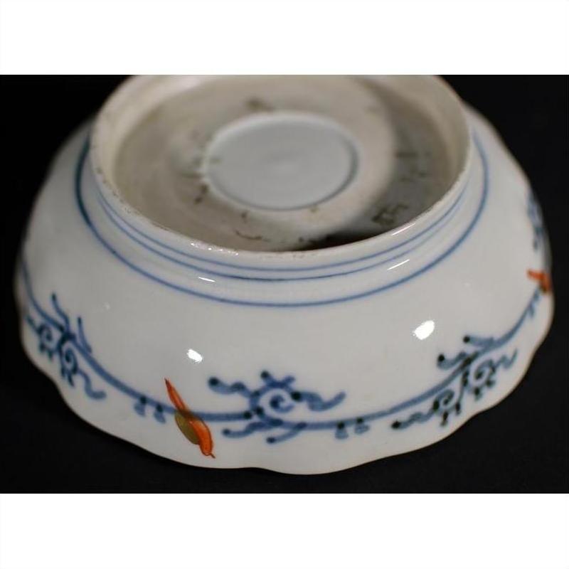 Blue and orange floral designs on white porcelain bowl, hand painted, seen on plain background.