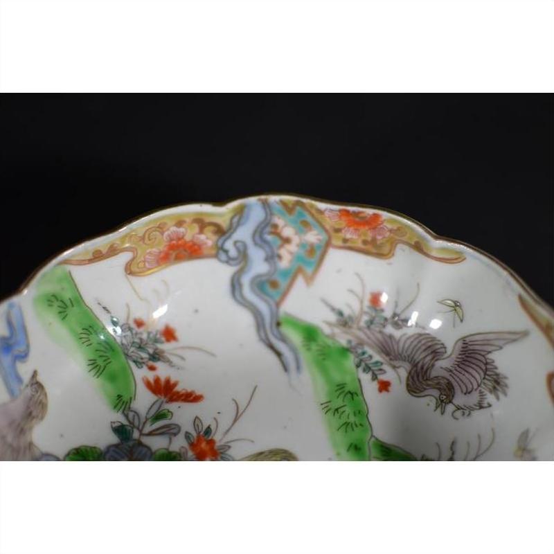 Close-up of a multicolored Imari porcelain bowl with scalloped rim, featuring gold, green, orange and blue floral and bird designs.