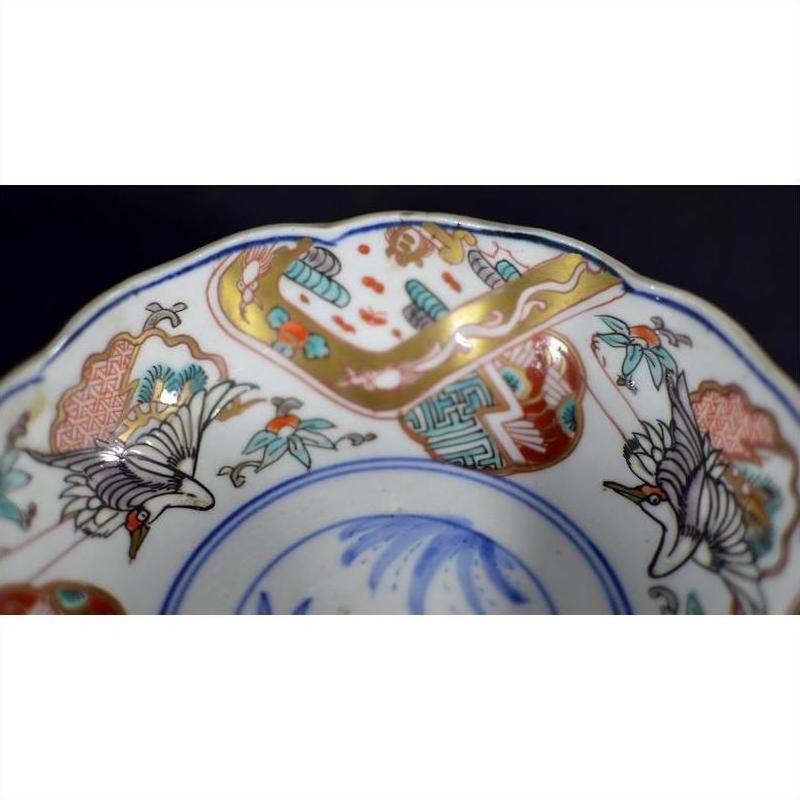 Close-up of a multicolor porcelain Imari bowl with hand painted cranes, floral patterns, and detailed edge designs.