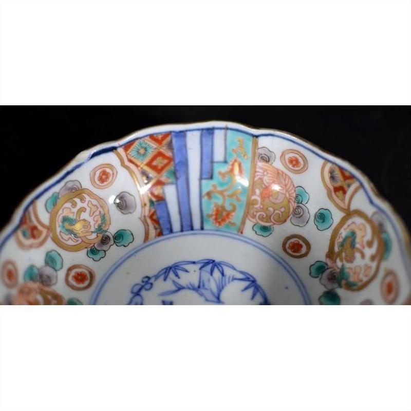 Close-up of a blue, red, green, and gold Imari porcelain bowl with hand-painted rim patterns.