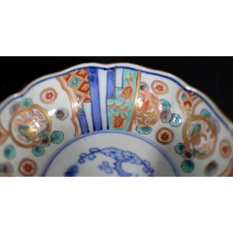 Close-up of a porcelain Japanese Imari bowl with vibrant red, blue, and green hand-painted patterns on the rim.