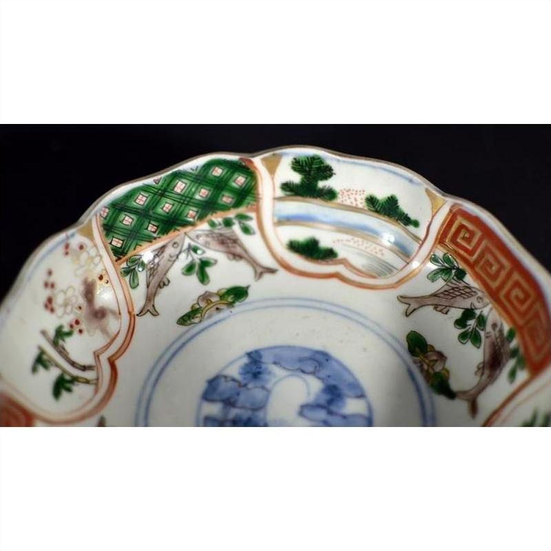 Close-up of an antique Japanese Imari porcelain bowl with green, orange, and blue bird, tree, and geometric patterns.