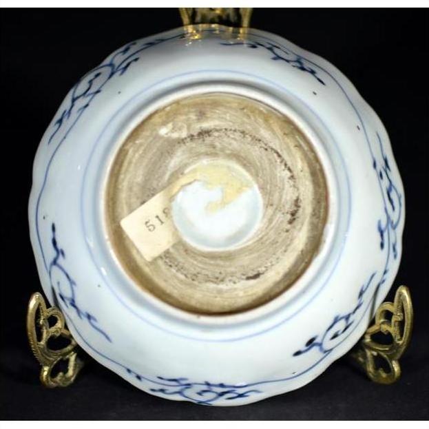 White and blue porcelain bowl base with sticker label on ornate metal stand, close-up.
