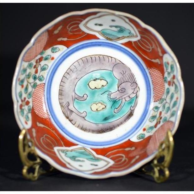 White and blue porcelain Imari bowl with hand painted dragon and cloud motifs on a decorative stand, close-up view.