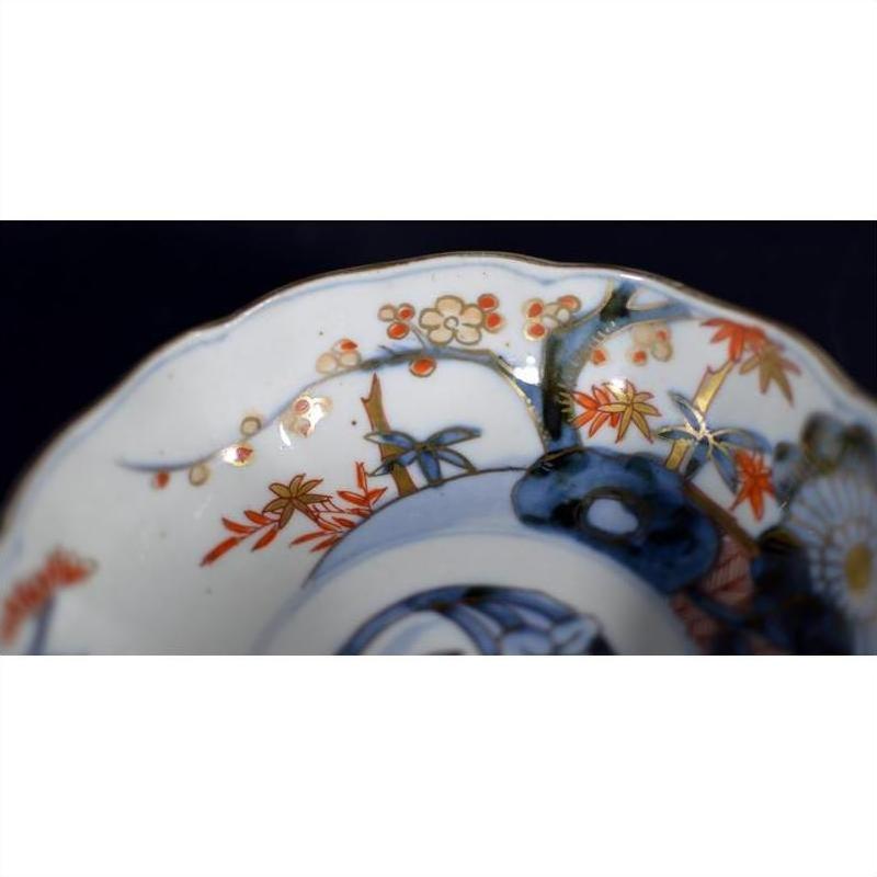 Close-up of a blue, orange, and gold porcelain Japanese Imari bowl with hand painted floral and tree motifs.