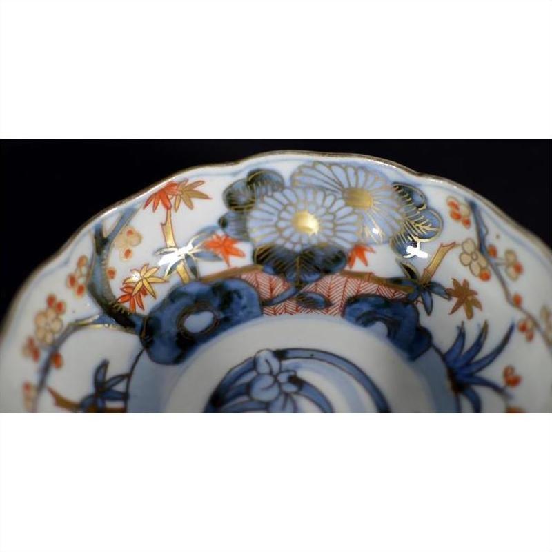 Blue, gold, and orange Imari porcelain bowl with hand painted floral and leaf patterns on rim, close-up.