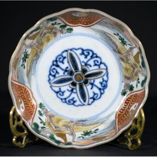 Close-up of antique Japanese Imari porcelain bowl with blue floral center and ornate gold, red, and green rim designs.