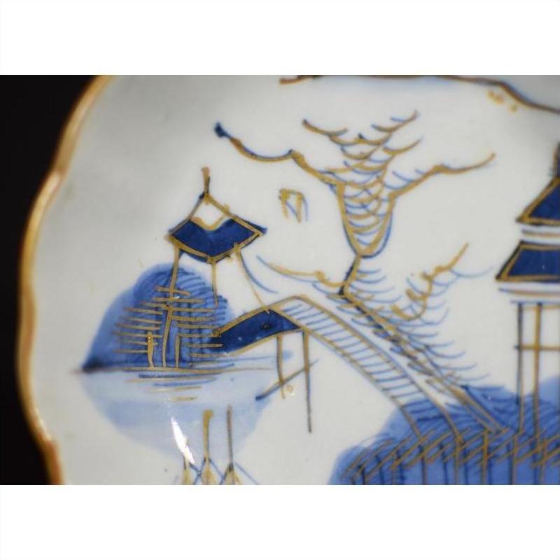 Close-up of blue and gold Imari porcelain plate featuring hand-painted pagoda, bridge, tree, and water.