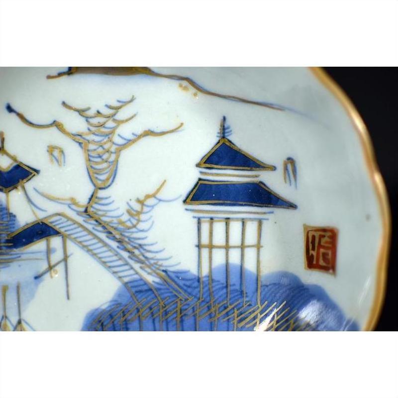 Close-up of blue and gold hand painted porcelain Japanese Imari plate with scenic landscape details.