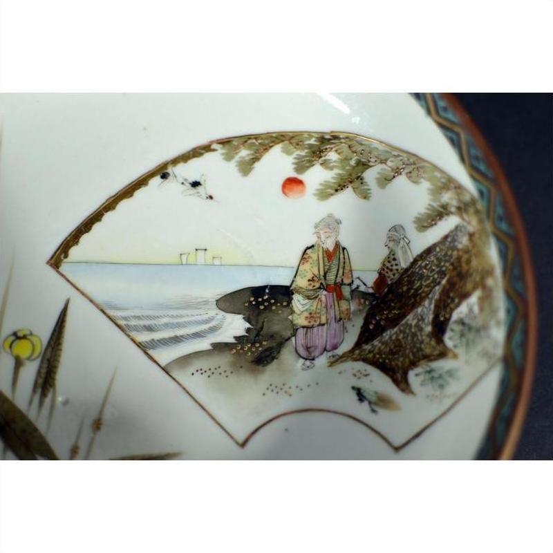 Close-up of antique hand-painted Japanese Kutani porcelain bowl with two figures, trees, red sun, and distant buildings.