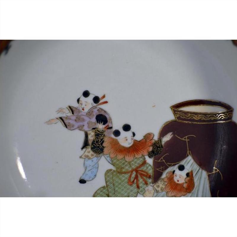 Close-up of an antique hand-painted Japanese Kutani porcelain plate with three figures in traditional dress near a large ornate vase.