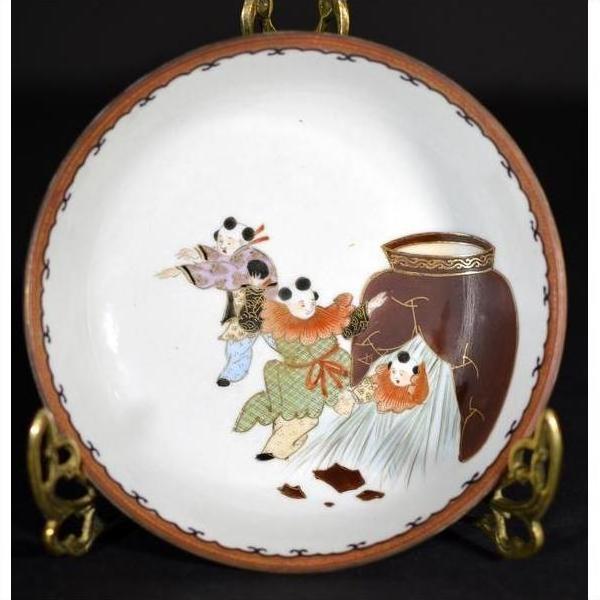 Close-up of antique Japanese Kutani porcelain plate, hand painted with three children in traditional dress by brown jar.