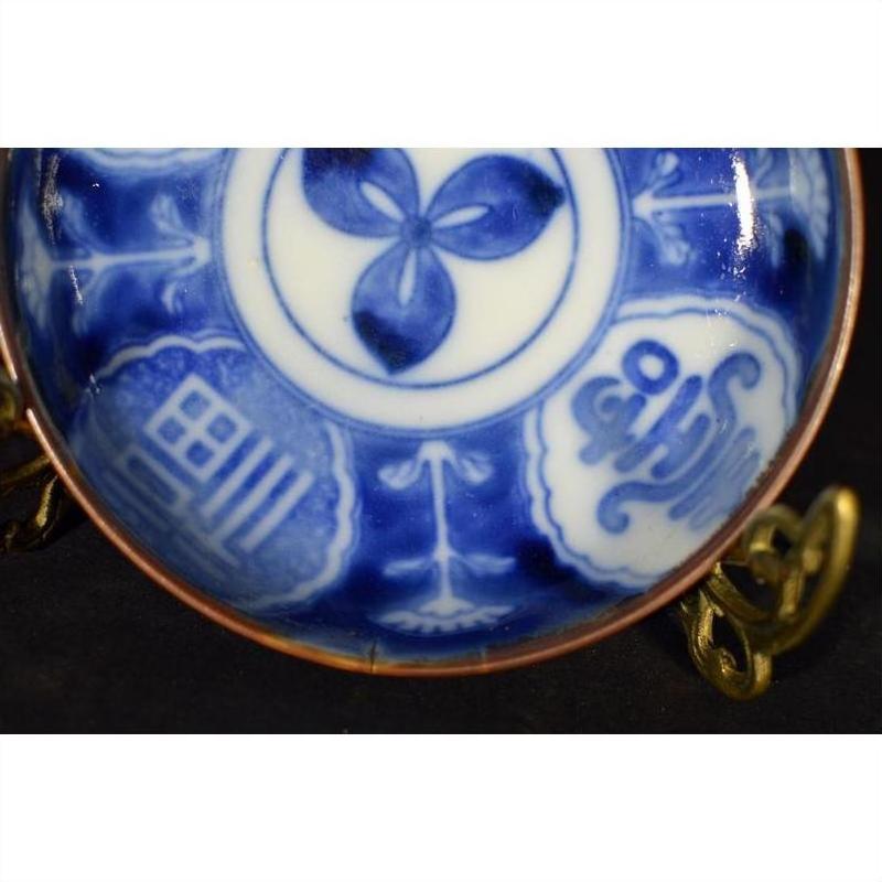 White porcelain Igezara transferware plate with intricate patterns and calligraphy on a brass stand.