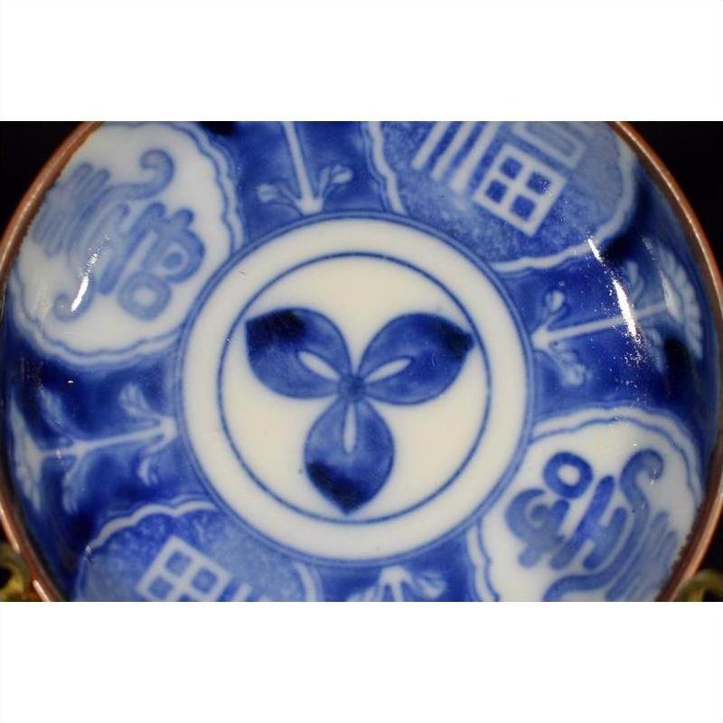 White porcelain Igezara transferware plate with central three-petal floral motif and abstract patterned rim, close-up.