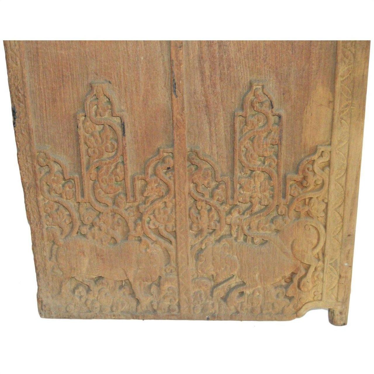 Brown Sheesham wood antique Indian door with carved animal and ornate foliage designs, close-up.