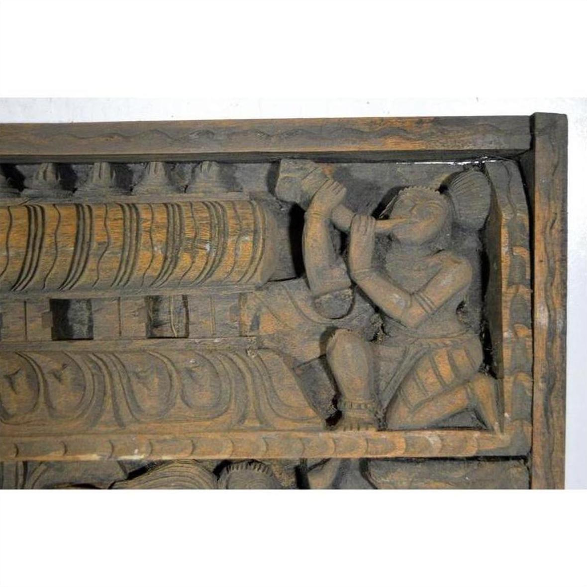 Brown Sheesham wood temple plaque with ornate carvings and kneeling figure blowing a horn, early 20th century.