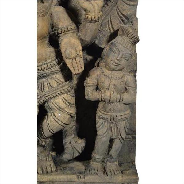 Brown sheesham wood temple decoration featuring a small stone figure with folded hands beside a larger figure’s limb.