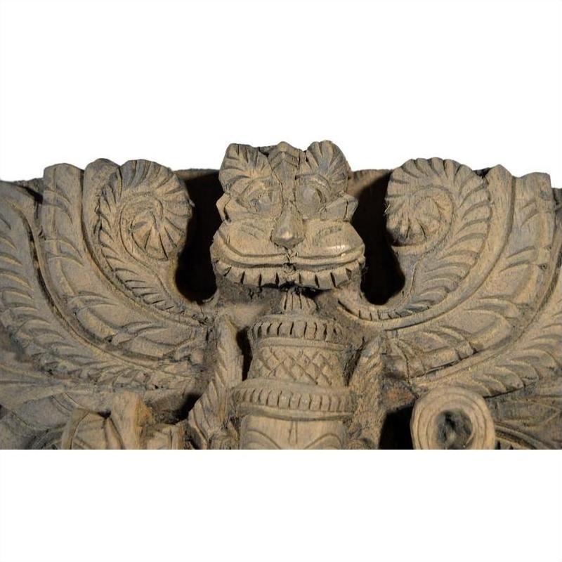 Brown sheesham wood hand-carved temple decoration with lion face and symmetrical leaf motifs, close-up view.