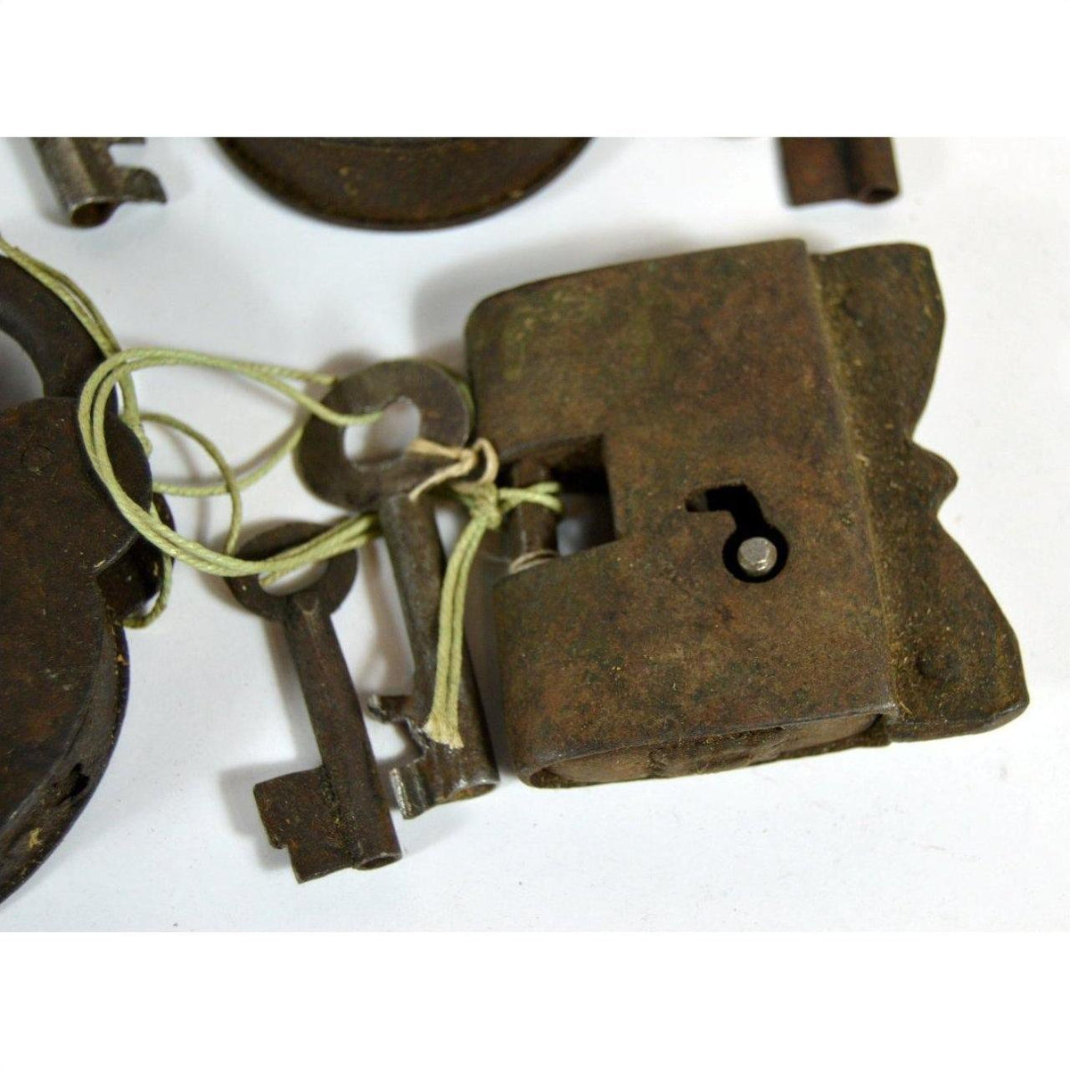 Close-up of an antique metal Indian lock with original keys tied by string, displayed on a white surface.