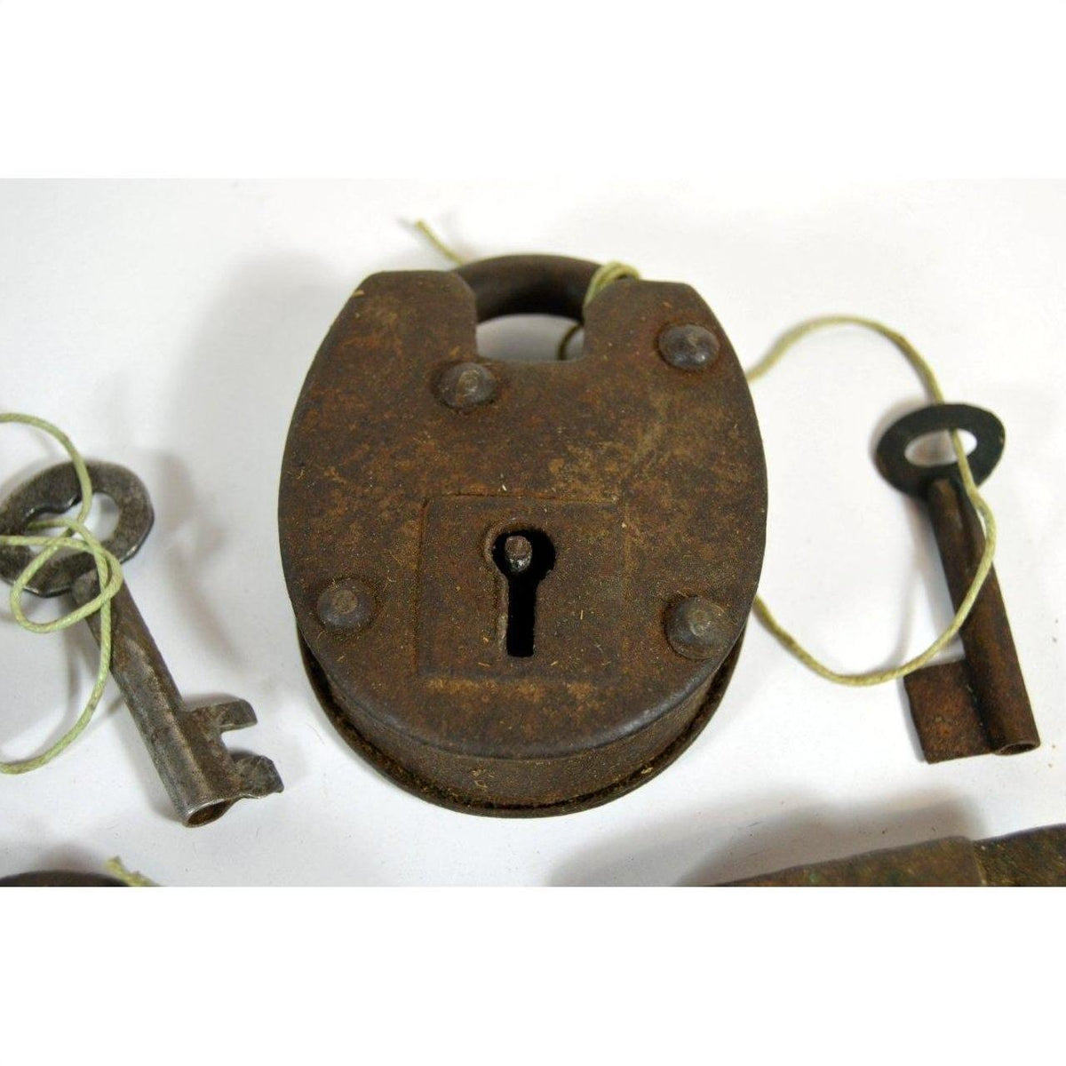 Close-up of antique metal Indian locks with original keys tied by string, displayed on a white surface.