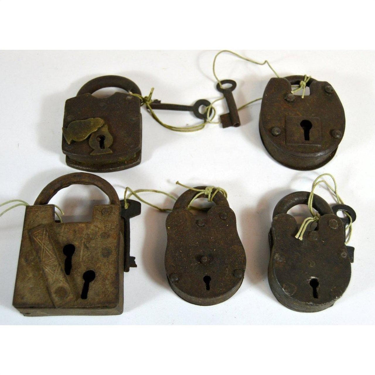 Close-up of five antique metal Indian locks with attached keys on strings, displayed on a white surface.