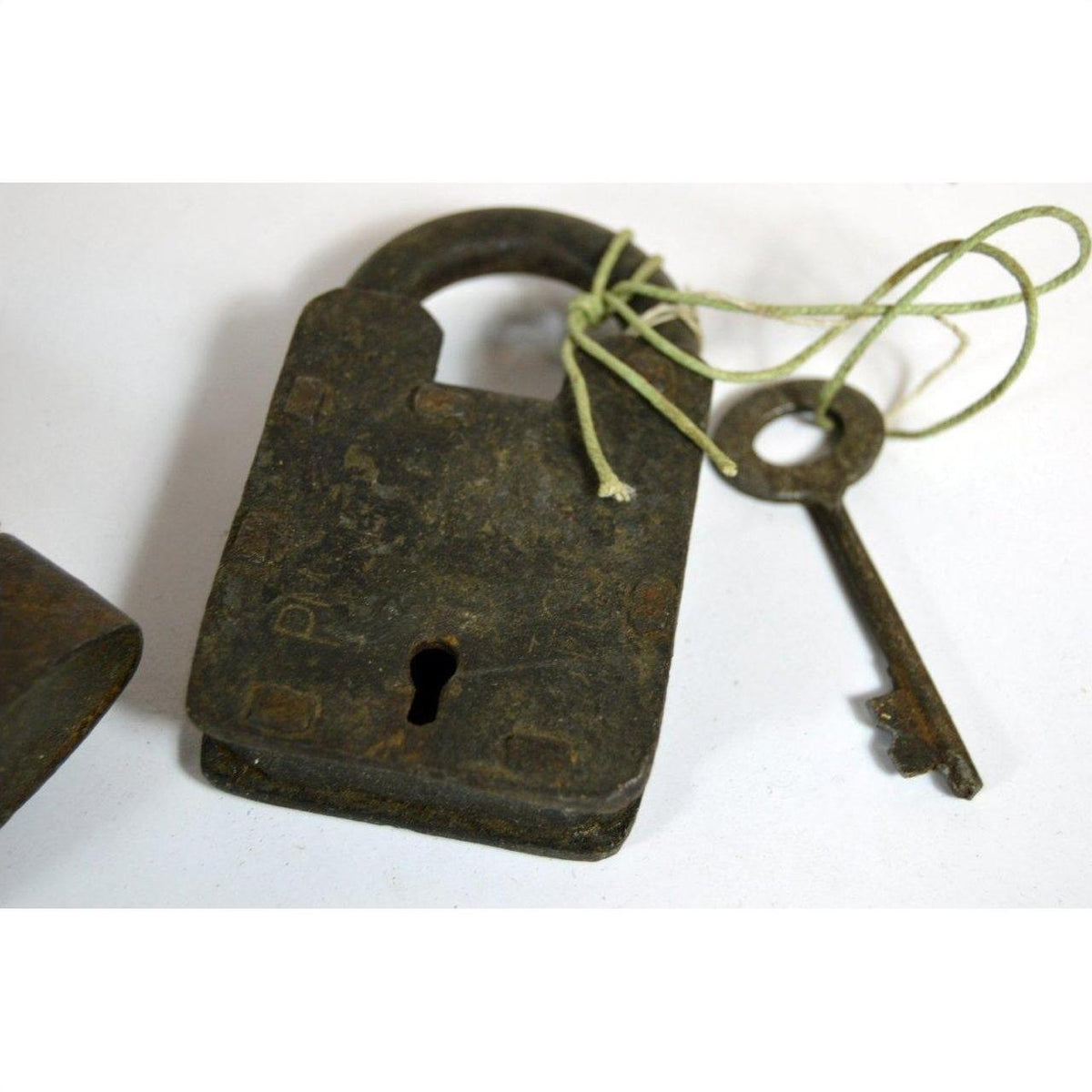 Close-up of an antique metal Indian lock with key tied by string, placed on a white surface.