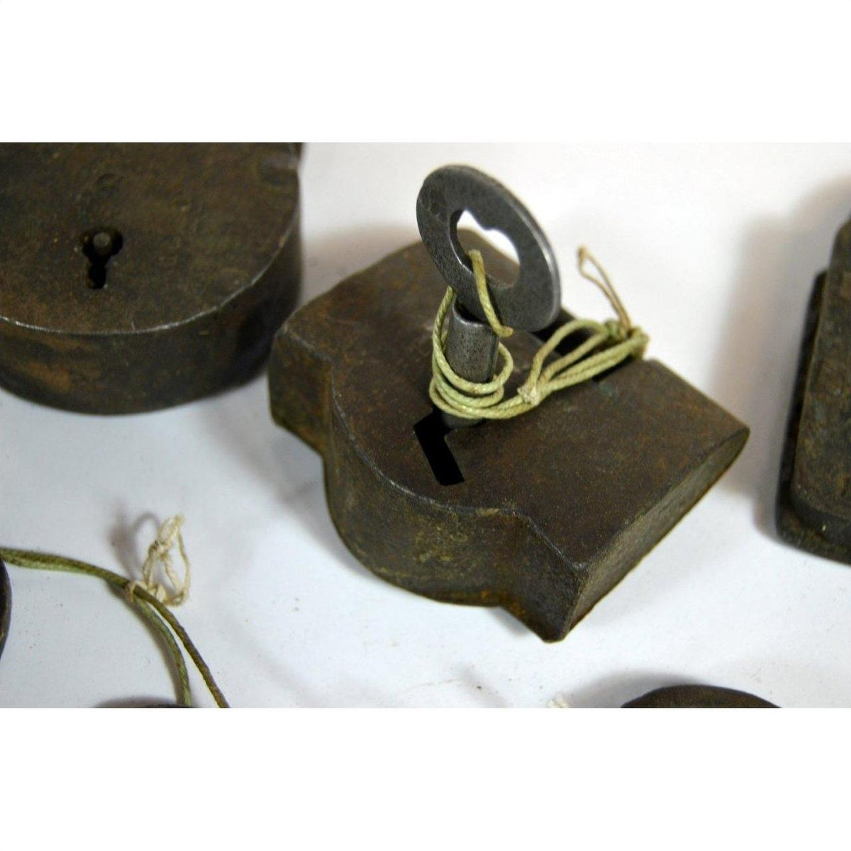Close-up of an antique metal Indian lock with an old key tied by string, resting on a white surface.