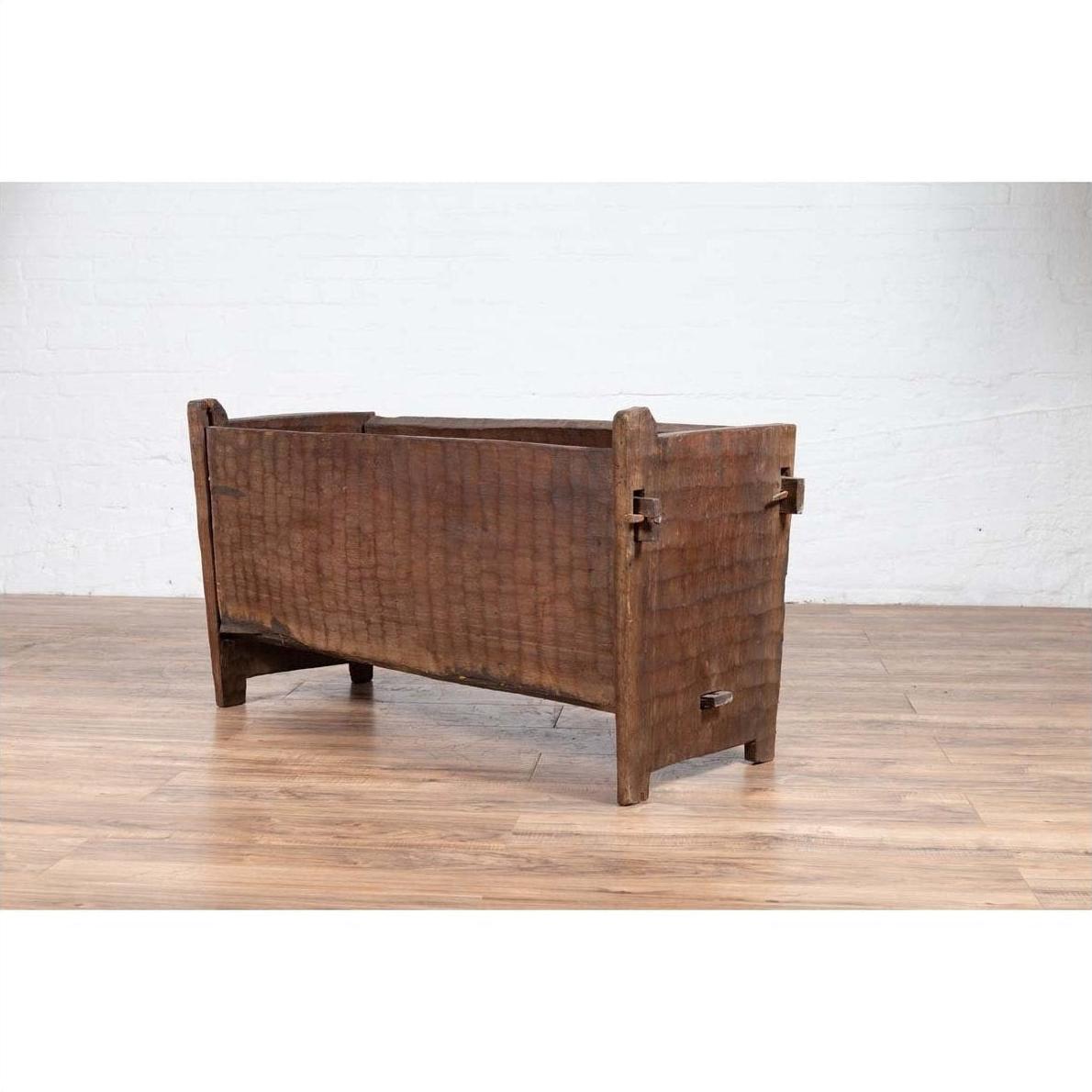 Weathered brown wooden planter with chiseled texture on a wooden floor against a white brick wall indoors.